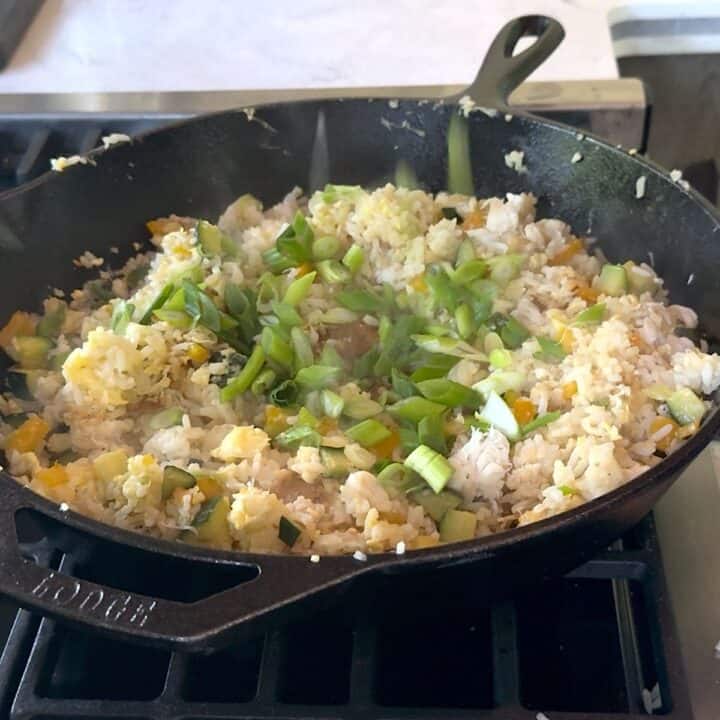 Adding the sliced green onion to the crab fried rice in a cast iron skillet.