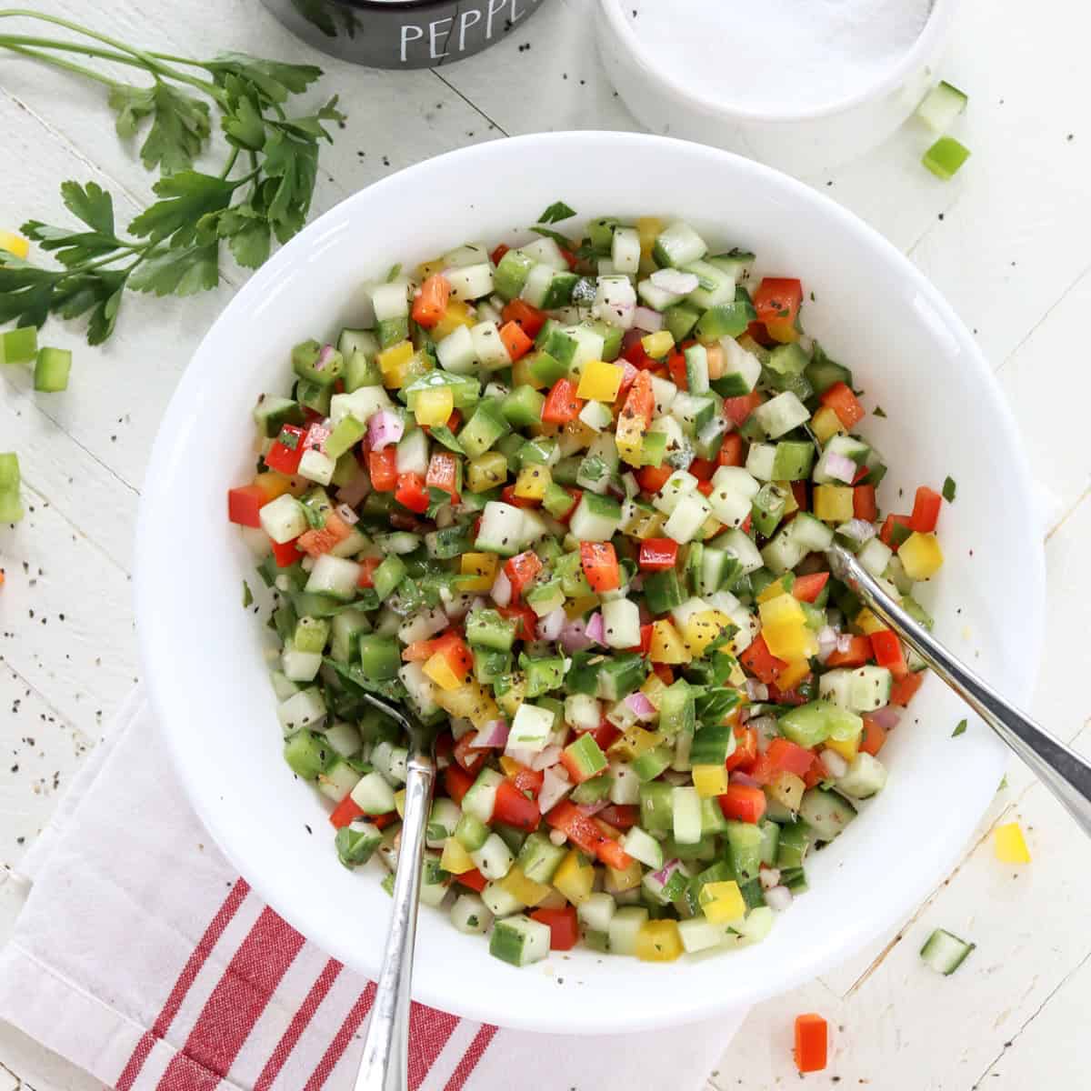 A white bowl of colorful cucumber and red bell pepper salad.
