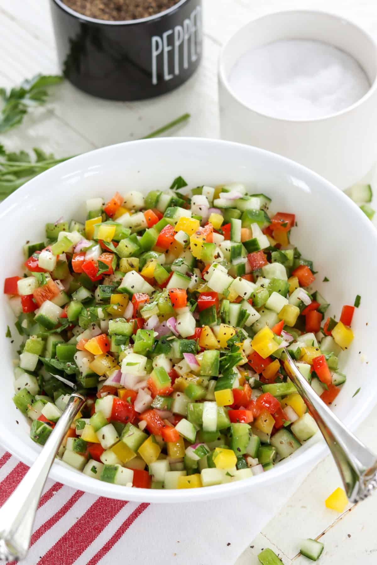Chopped bell pepper cucumber salad in a white round bowl with serving spoons.