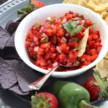 Strawberry salsa in a white bowl with a jalapeno and tortilla chips on the side.