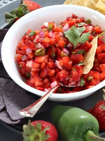Strawberry salsa in a white bowl with a jalapeno and tortilla chips on the side.