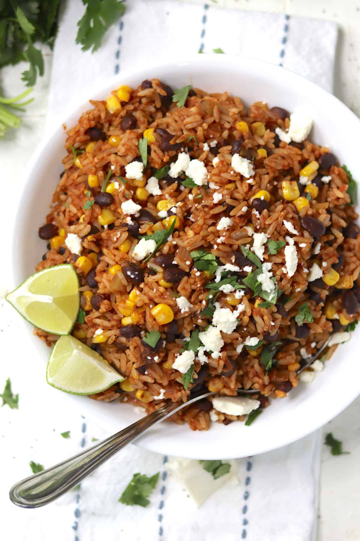 Mexican fried rice garnished with cilantro, lime wedges, and queso fresco cheese.