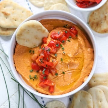 Homemade smoky red bell pepper hummus in a white bowl with a cracker for dipping.
