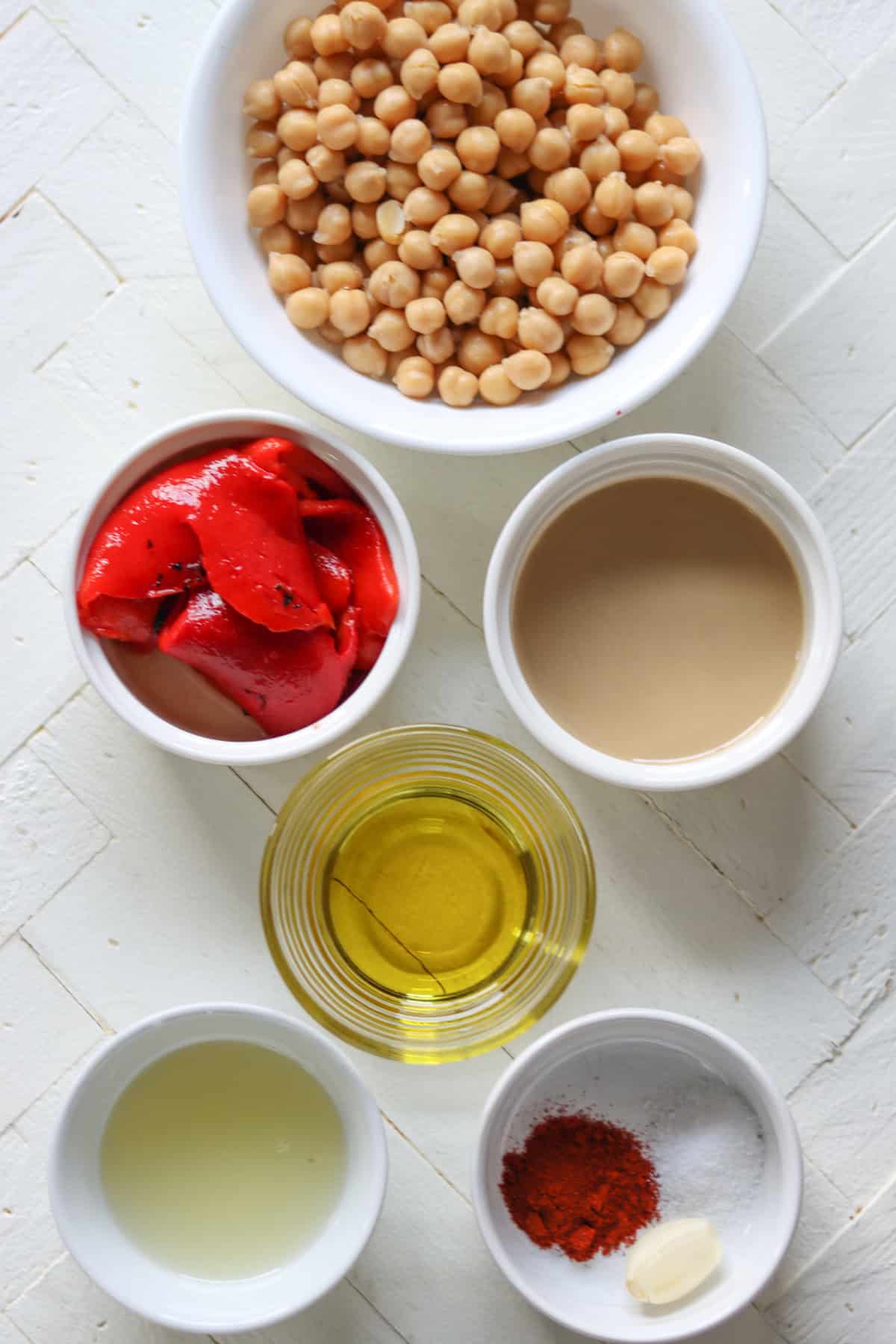 Ingredients needed for making red bell pepper hummus on a white board.