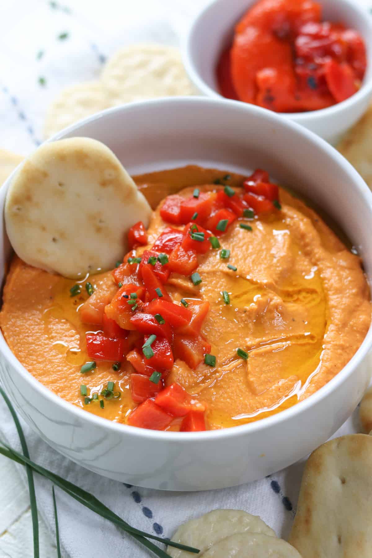 A white bowl of hummus with a naan bite for dipping.