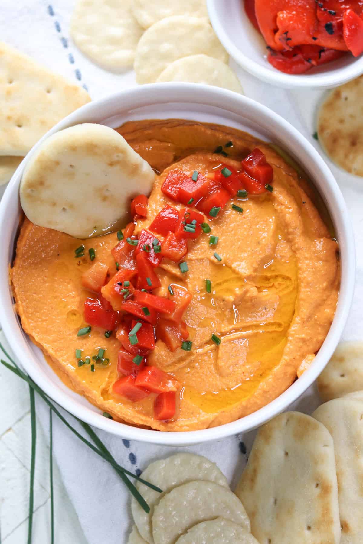 Red bell pepper hummus in a white bowl with crackers and naan bites.