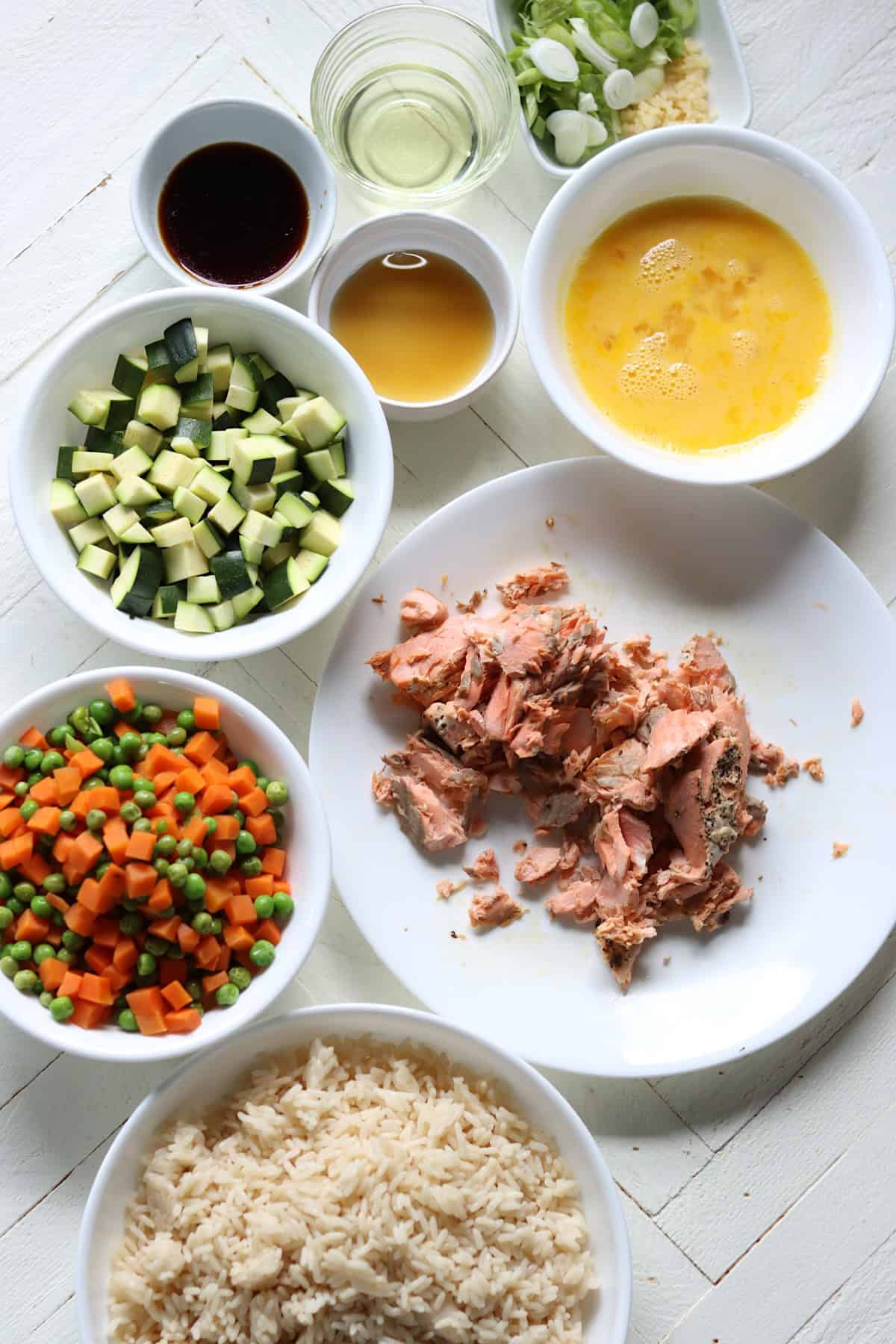 Ingredients needed for making salmon fried rice on white wooden board.