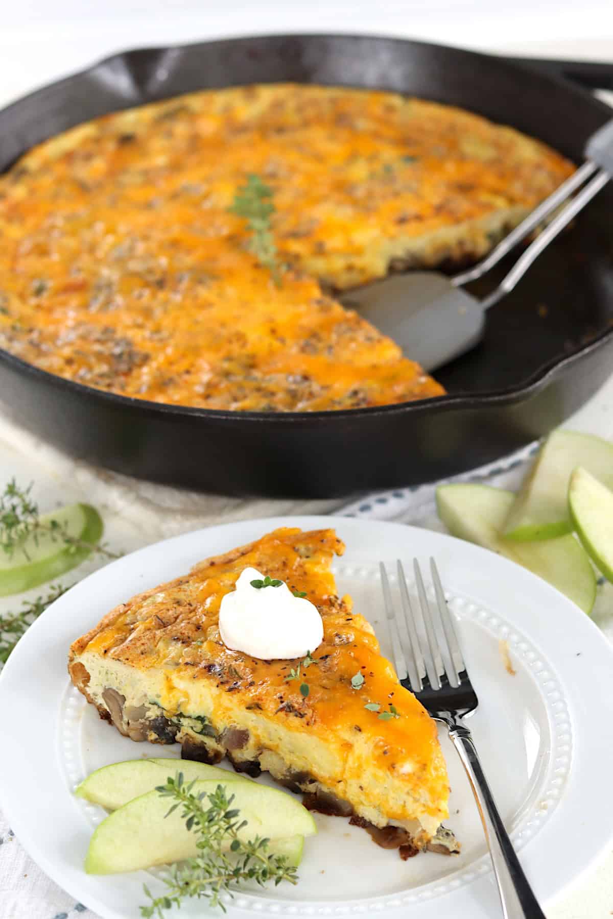 A sliced of apple and cheddar egg frittata on a white plate with apple slices.