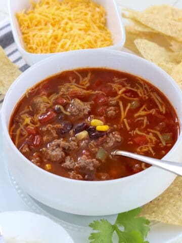 White bowl of beef enchilada soup with shredded cheese.
