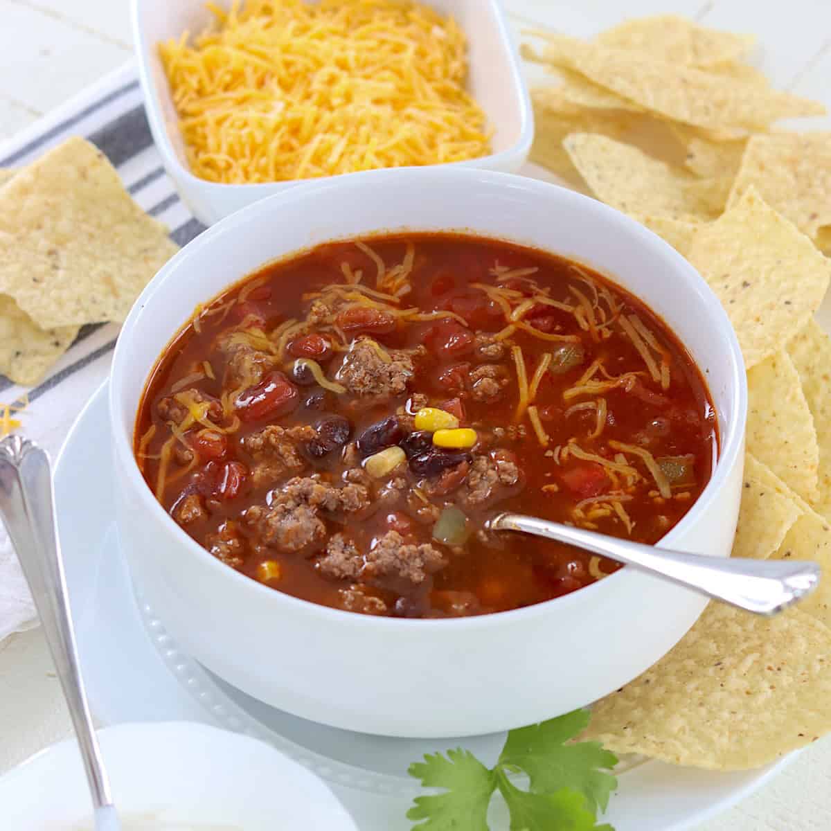 White bowl of beef enchilada soup with shredded cheese.