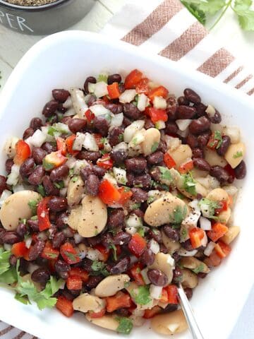 Tossed black bean salad with butter beans and cilantro in a white bowl.