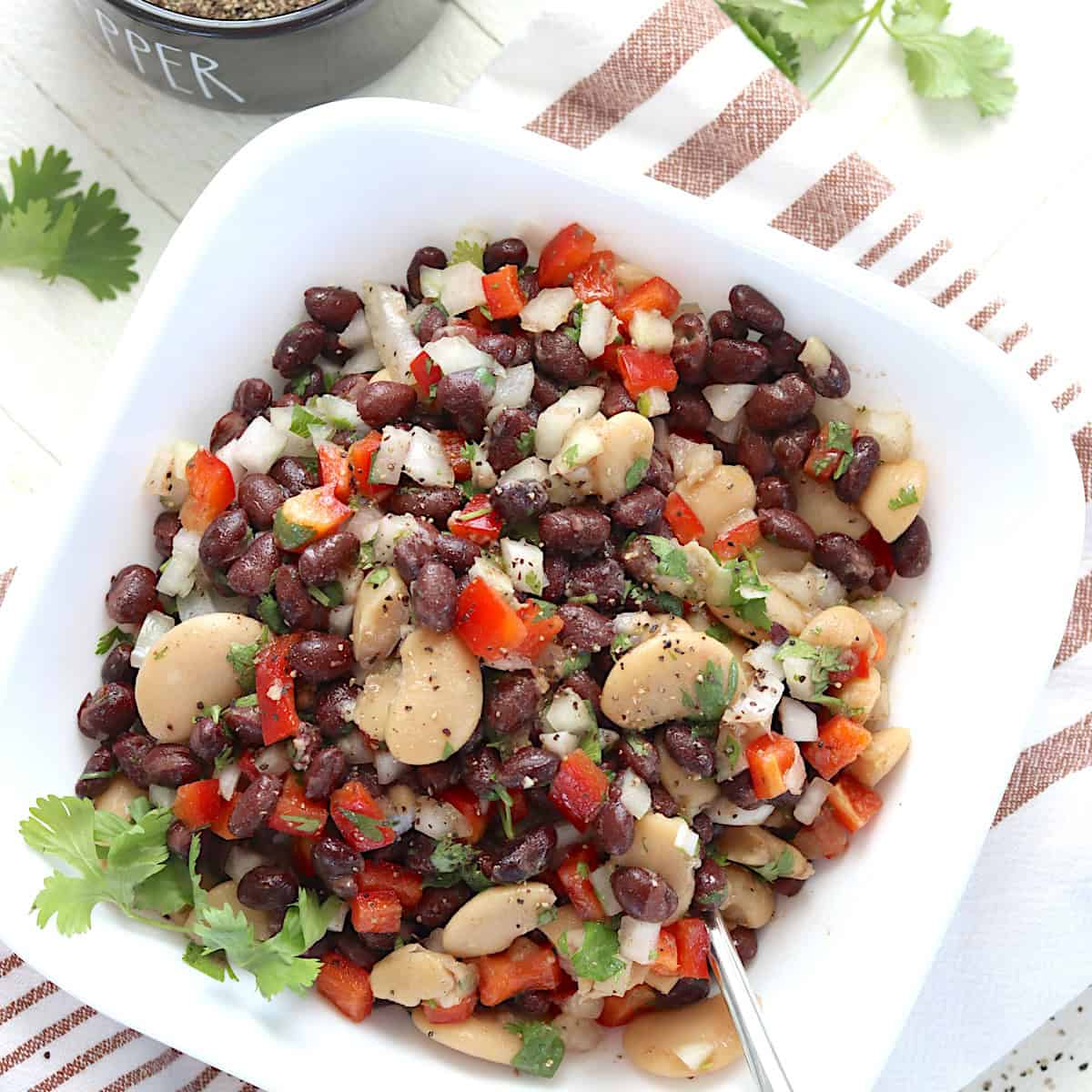 Tossed black bean salad with butter beans and cilantro in a white bowl.
