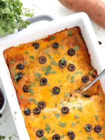 Baked cheesy sweet potato and black bean enchiladas baked in a white casserole dish.