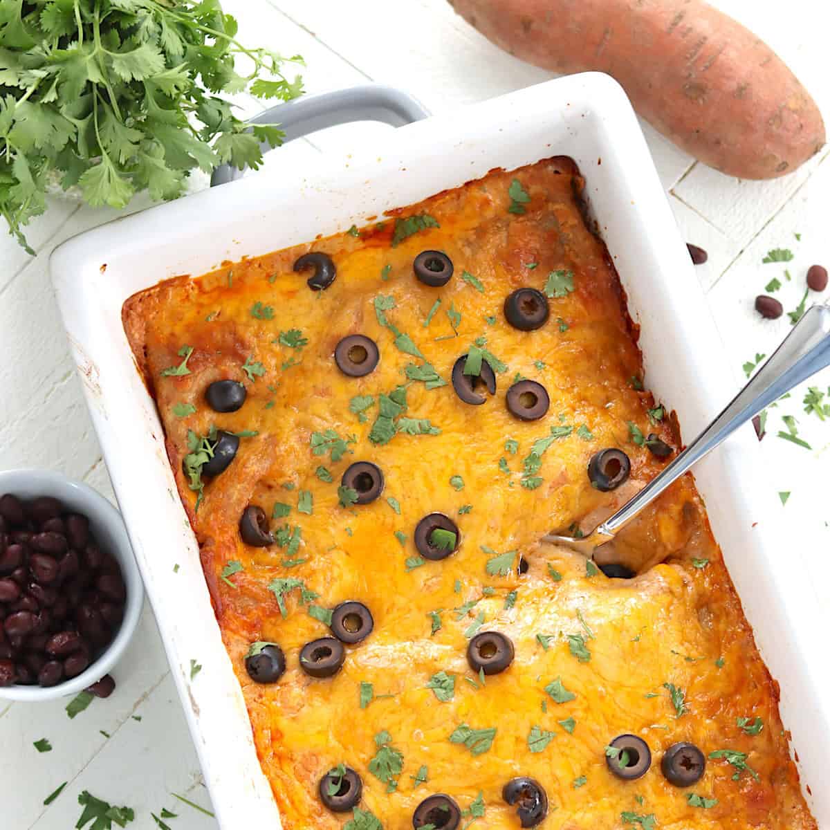 Baked cheesy sweet potato and black bean enchiladas baked in a white casserole dish.