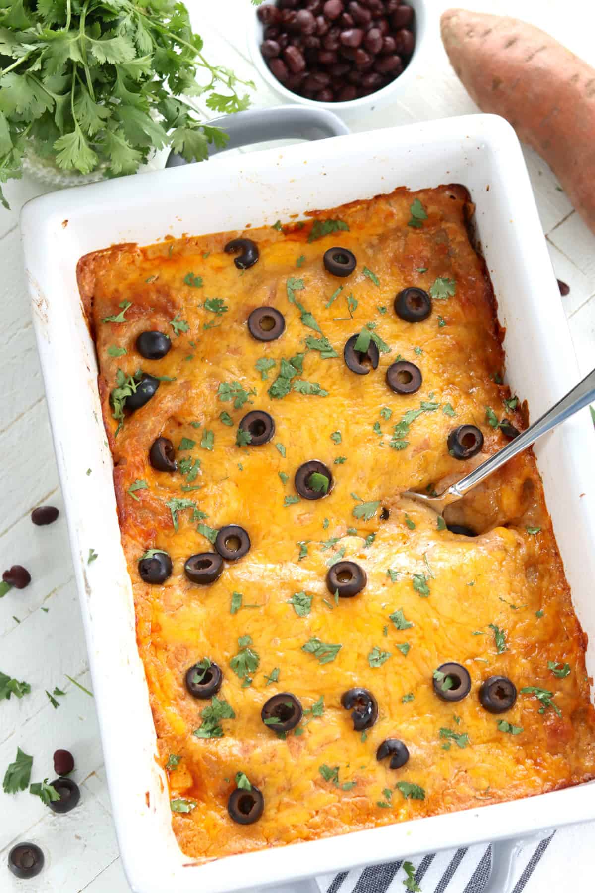 A gray and white rectangle casserole dish with black beans sweet potato casserole topped with black olives.