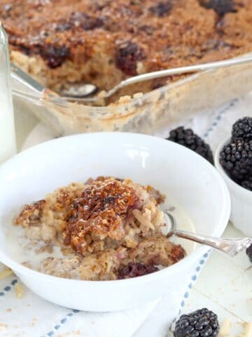 A white bowl of baked blackberry oatmeal topped with non dairy cream and brown sugar sprinkles.