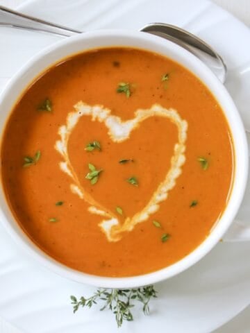 Coconut curry pumpkin soup in a white handled bowl with drizzled in a heart shape.
