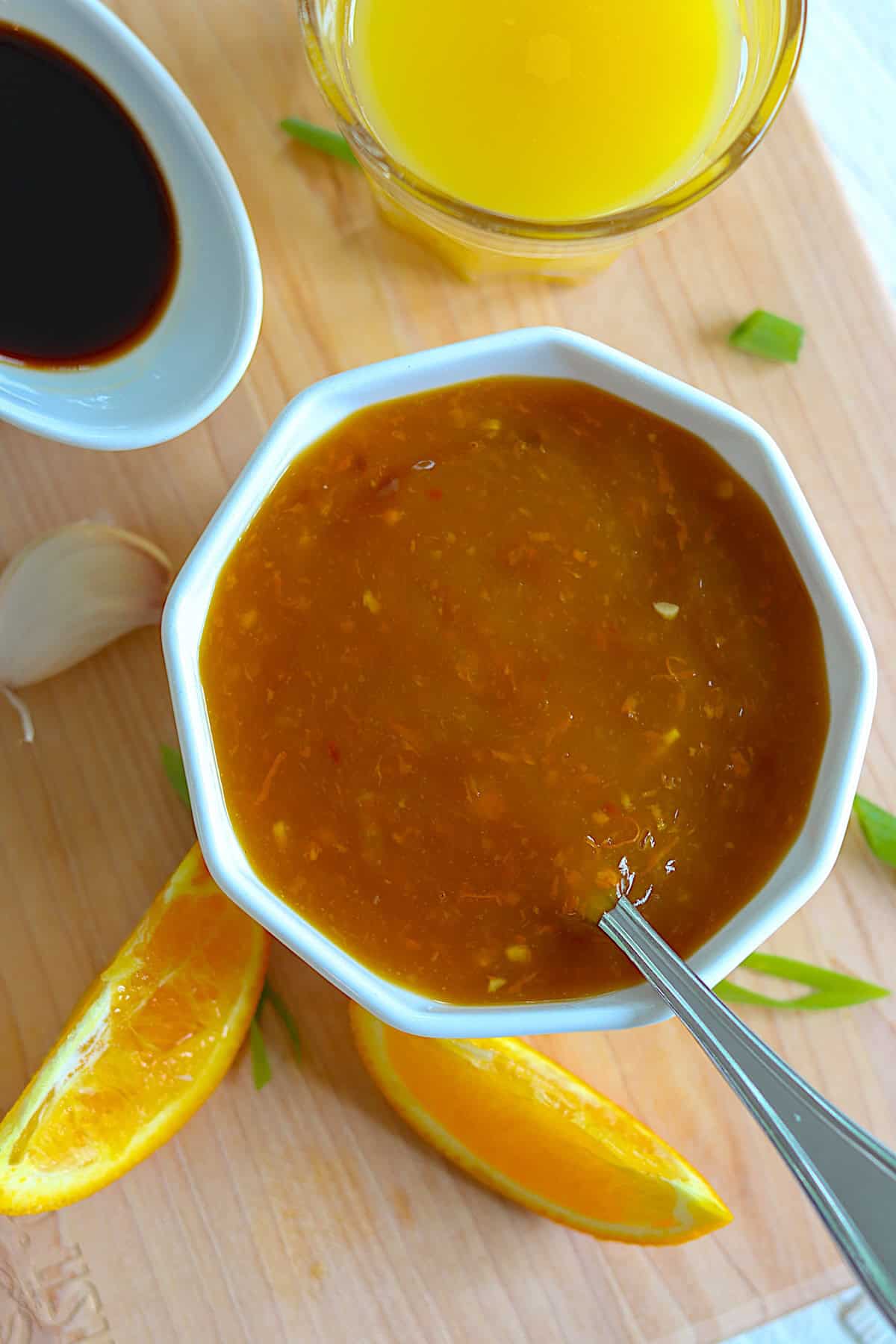 A white bowl of orange sauce on a wood board with orange slices.
