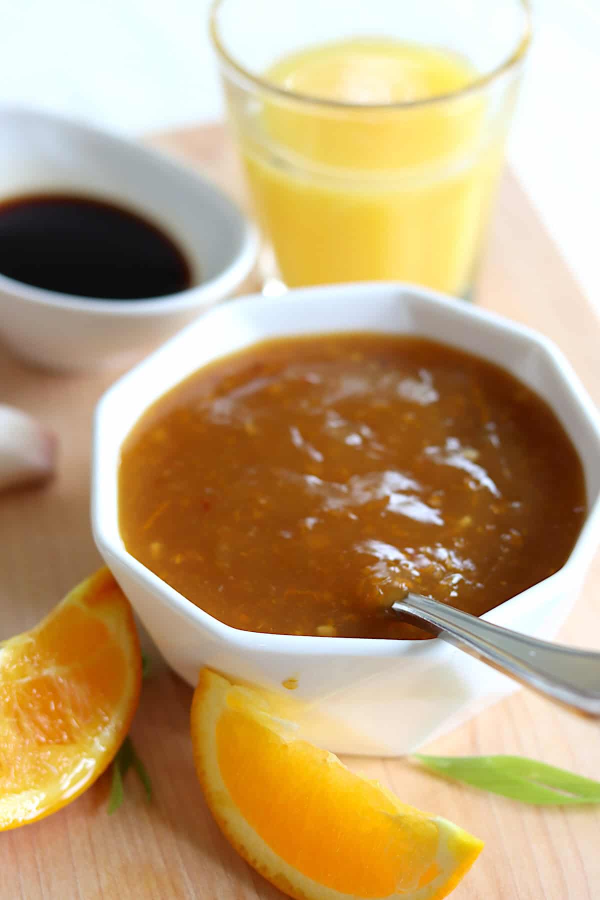 A small white bowl of orange sauce for chicken with a glass of orange juice in the background.