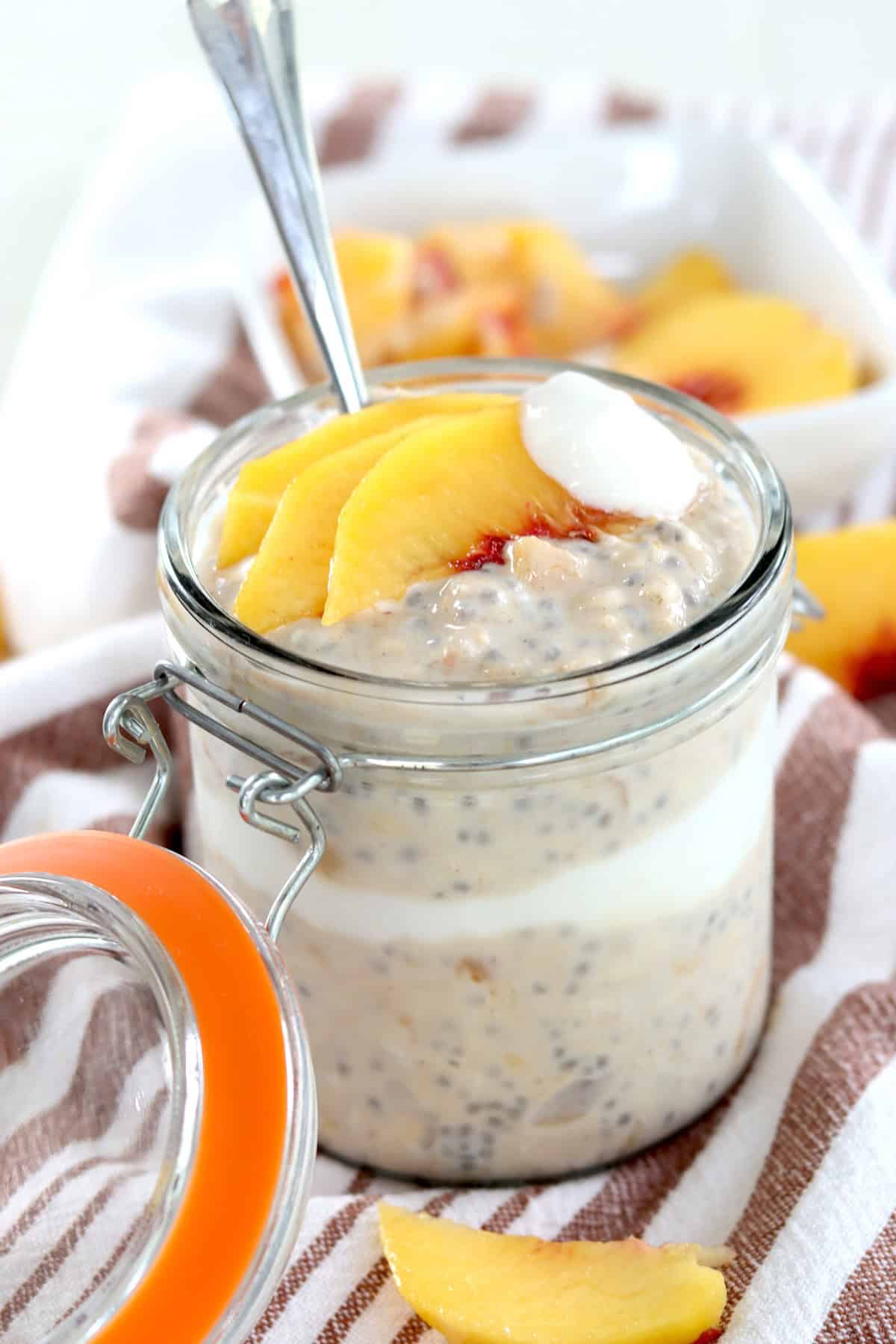 A clear lidded jar layered with overnight peach oatmeal yogurt and peaches.