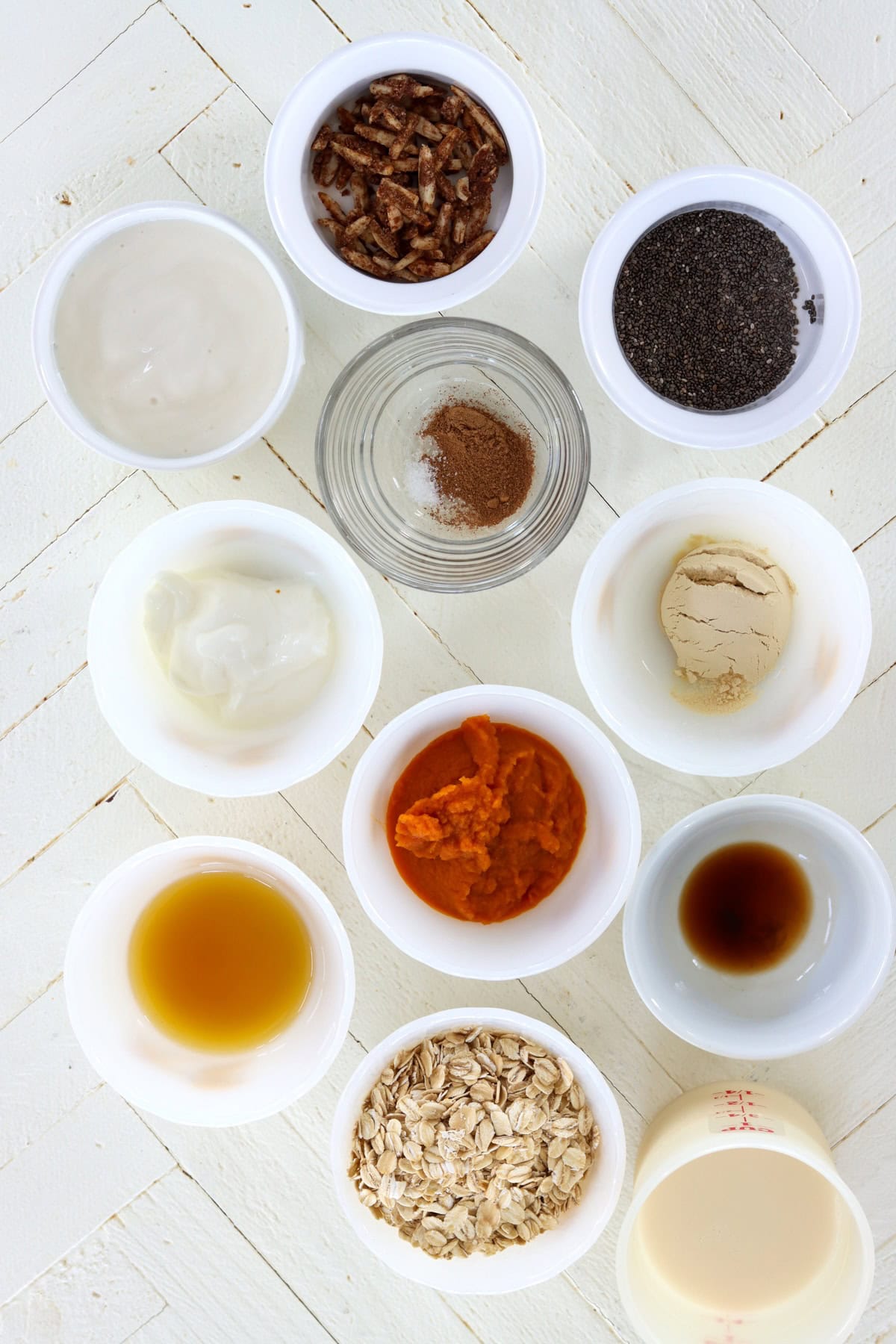 Ingredients needed for making pumpkin overnight oats on a white wooden board.