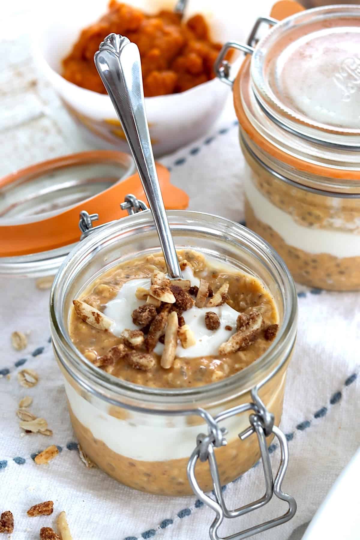 A glass jar layered with pumpkin pie overnights oats, maple yogurt swirl and topped with toasted candied almonds.