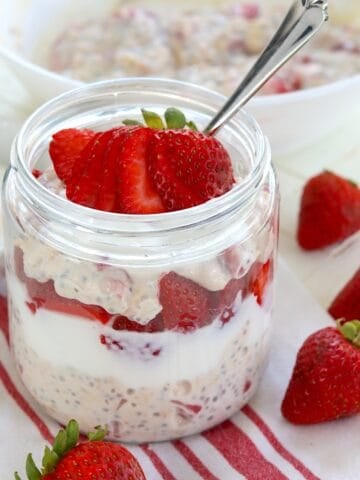 A clear glass jar layered with strawberries and cream overnight oats, strawberries, and yogurt.