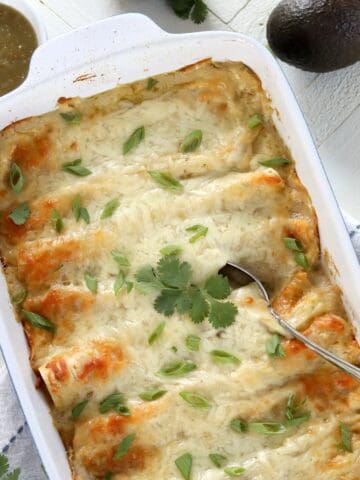 A rectangle white backing dish of vegan enchiladas with green chili sauce.