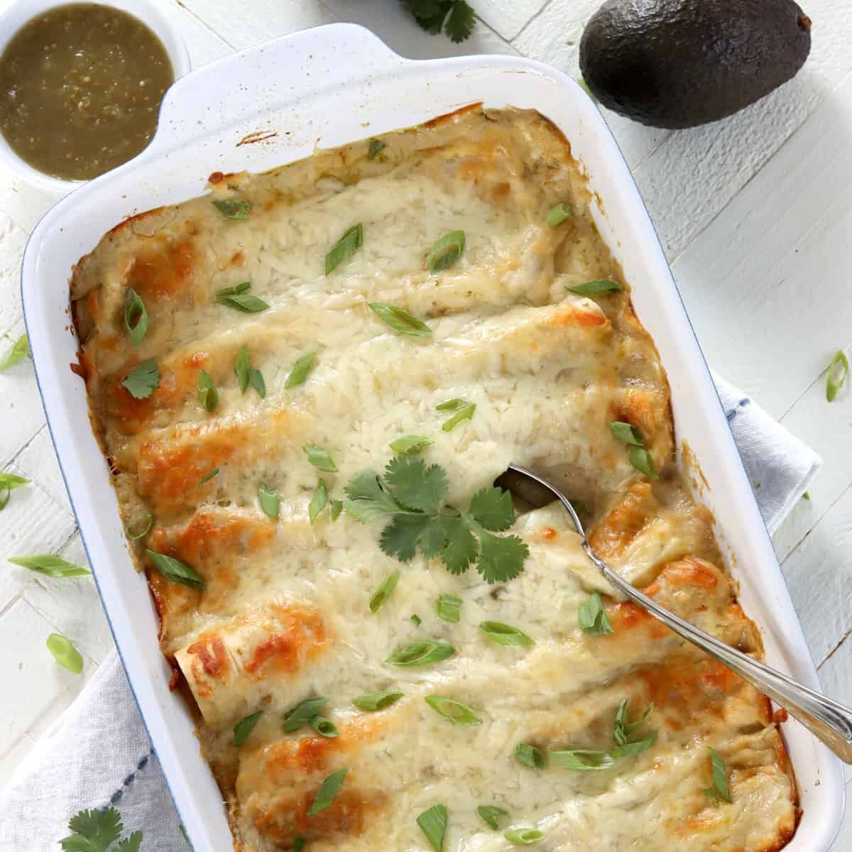A rectangle white backing dish of vegan enchiladas with green chili sauce.