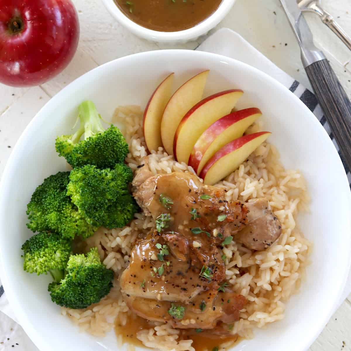 Two apple cider glazed chicken thighs in a white shallow bowl with rice.