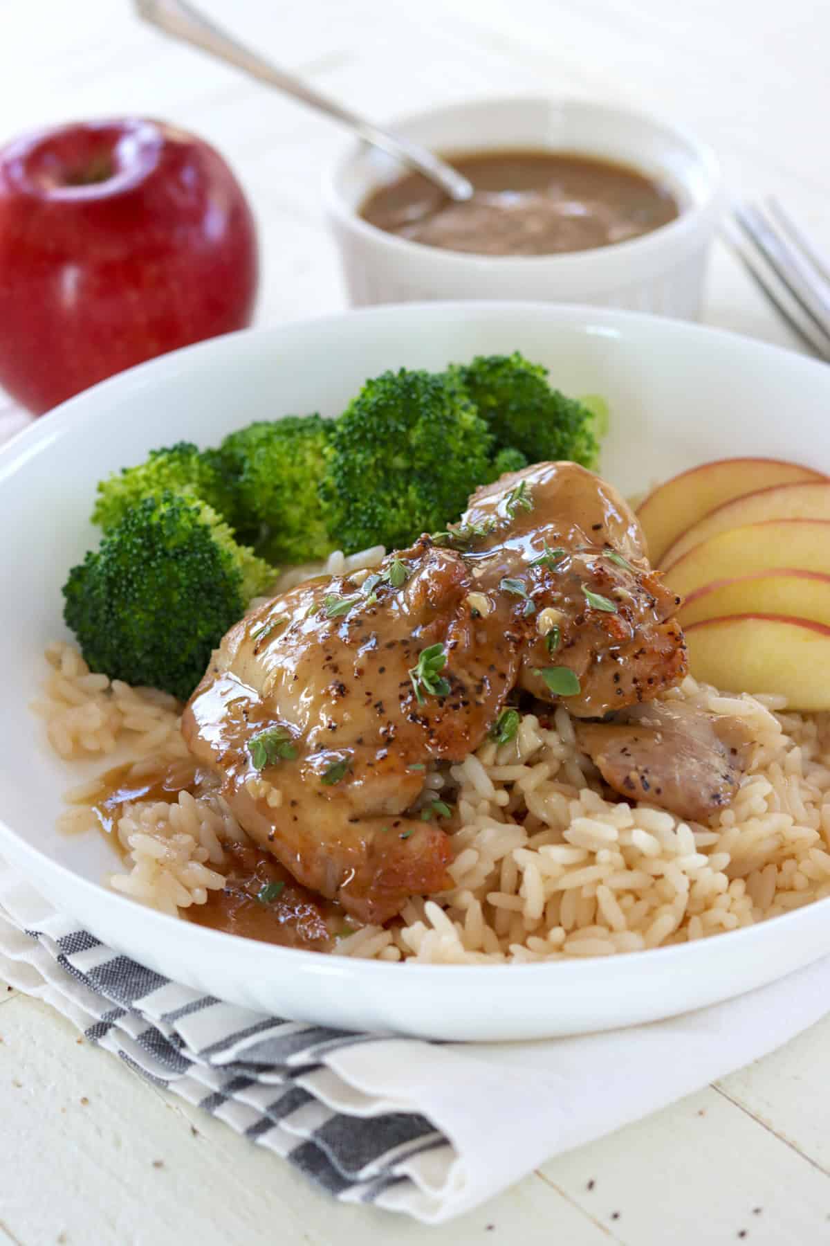 A white plate with apple cider glazed chicken thighs over rice with steamed broccoli.