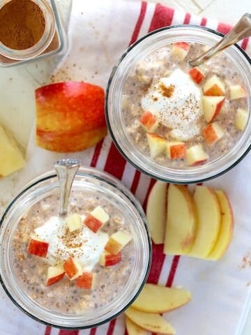 Two clear glass jars of apple cinnamon overnight oats with diced apple on top.