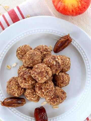 Apple cinnamon energy bites on a white plate with dates and an apple.