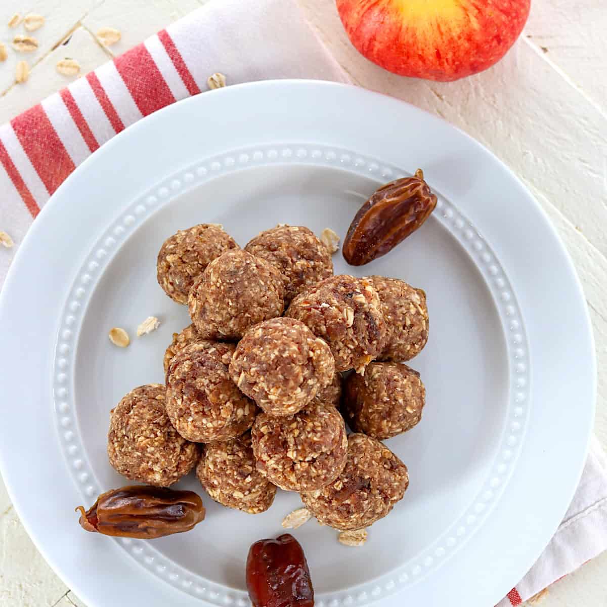 Apple cinnamon energy bites on a white plate with dates and an apple.
