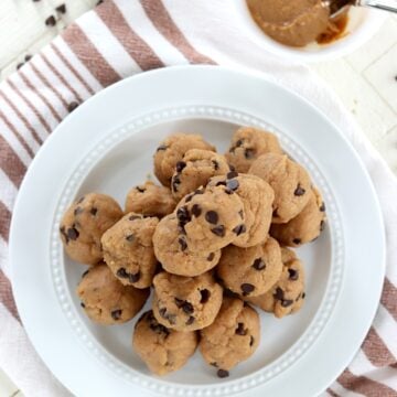 A white round plate of chocolate chip peanutu butter protein balls with a side of peanut buter.