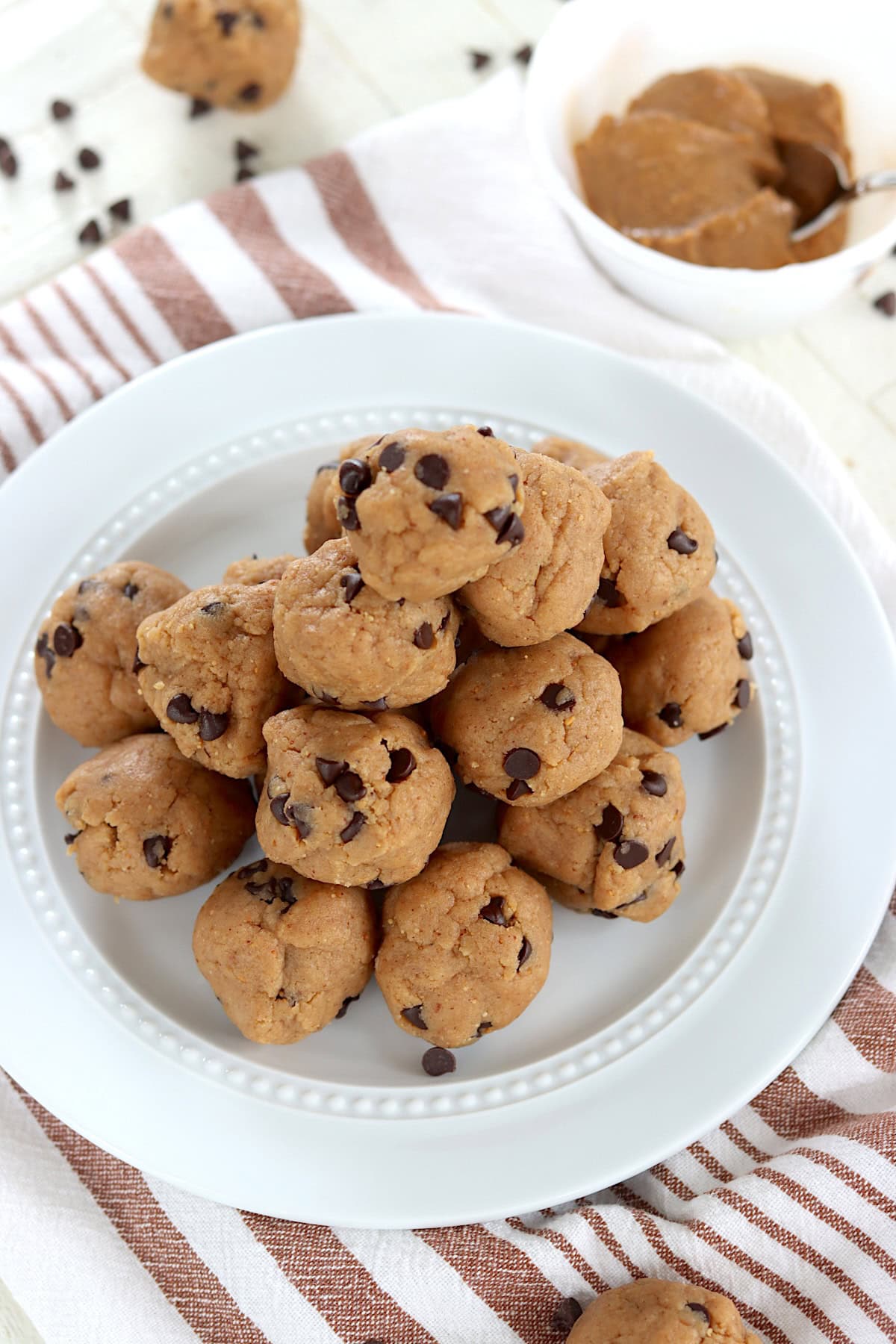 Peanut butter and chocolate chip protein balls piled on a white plate over a striped napkin.