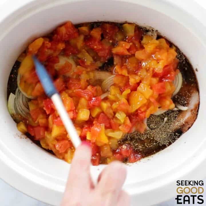 Crock pot balsamic chicken with boneless skinless chicken thighs balsamic vinegar and veggies layered in a white oval slow cooker.