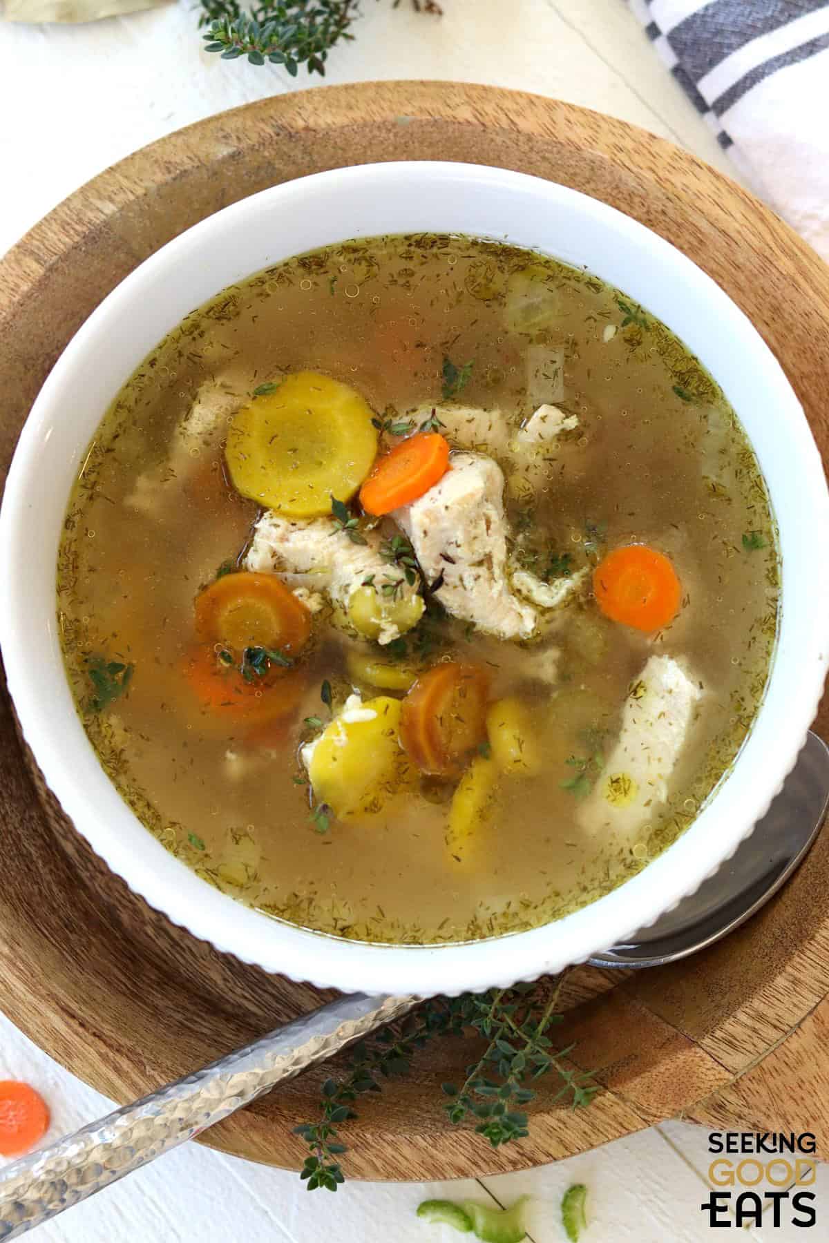 Instant pot chicken soup in a white bowl on a wooden charger.