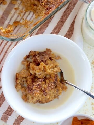 Pumpkin baked oatmeal in a white bowl with a spoon and a splash of milk.