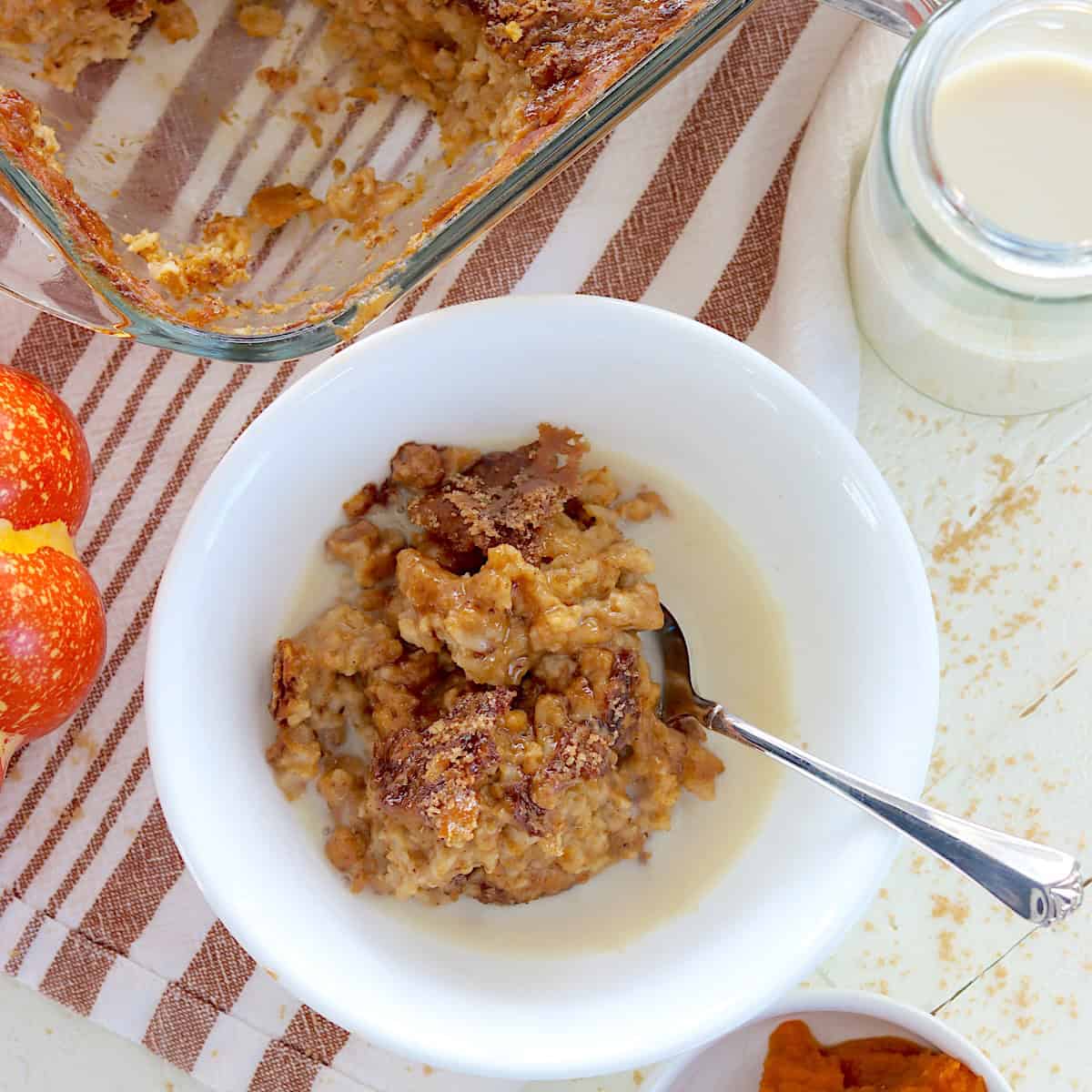 Pumpkin baked oatmeal in a white bowl with a spoon and a splash of milk.