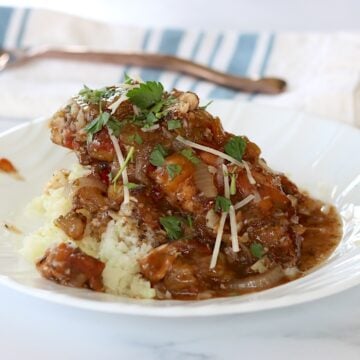 A white plate of crockpot balsamic chicken over cauliflower.