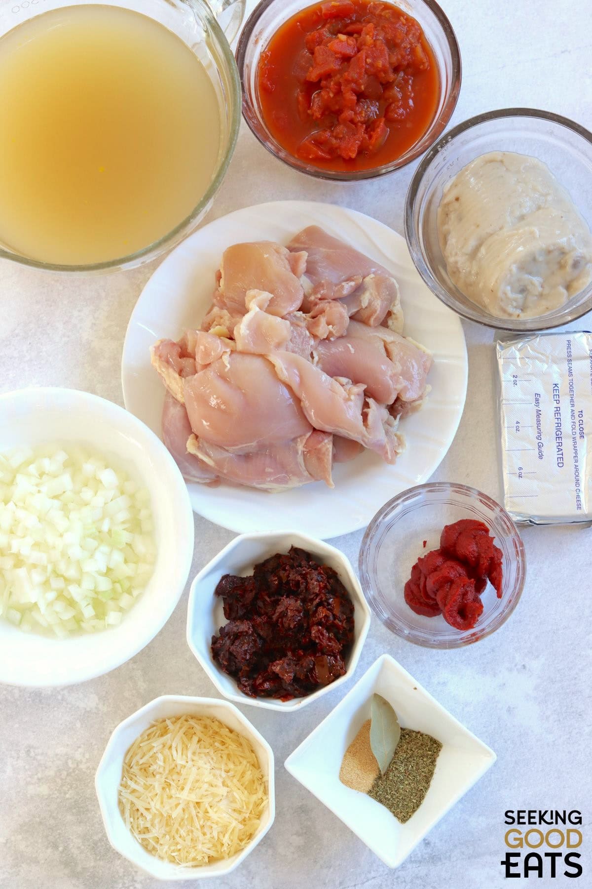 Ingredients needed for making tomato chicken soup on a white board.