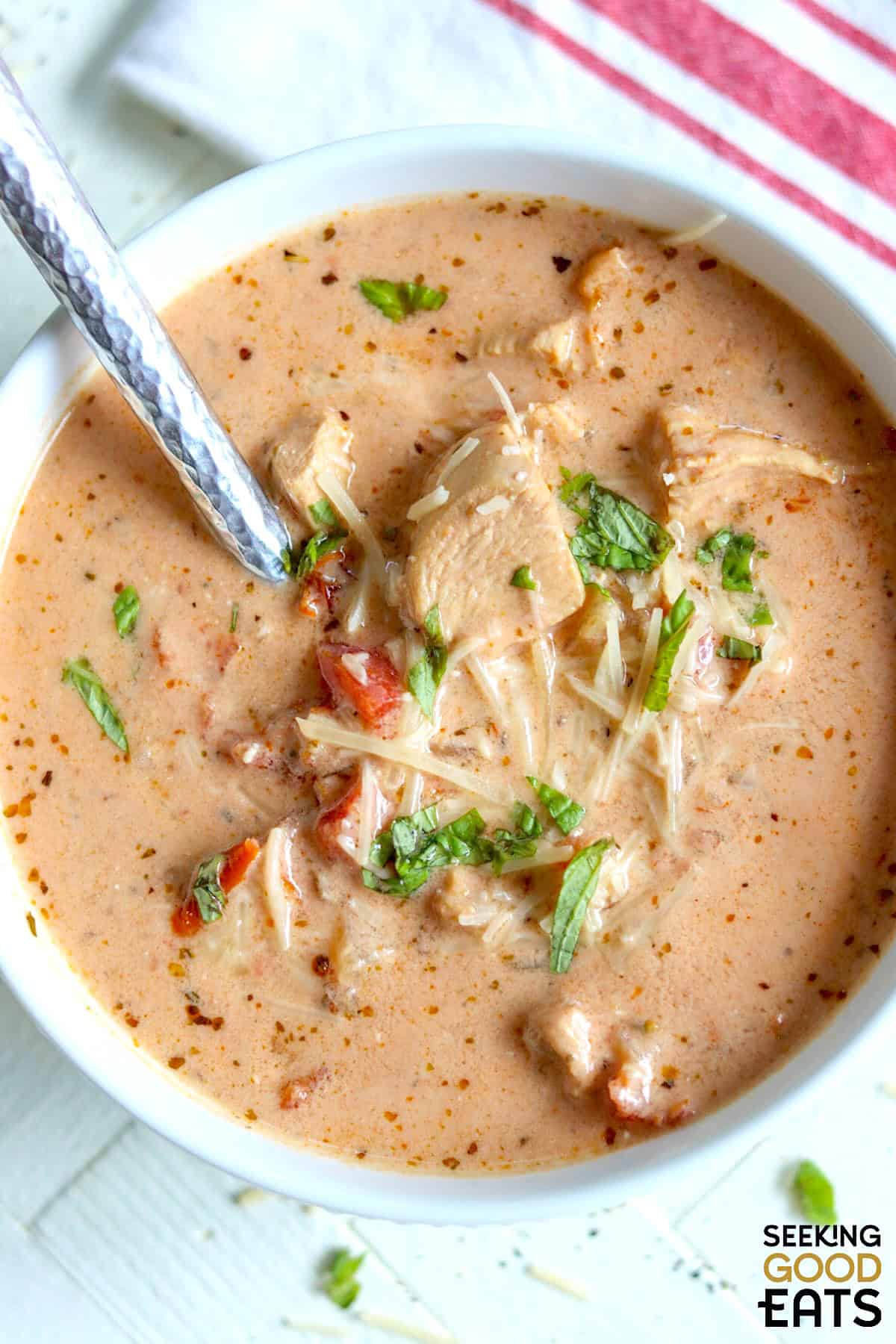 A round white bowl of creamy sun-dried tomato chicken soup garnished with parmesan