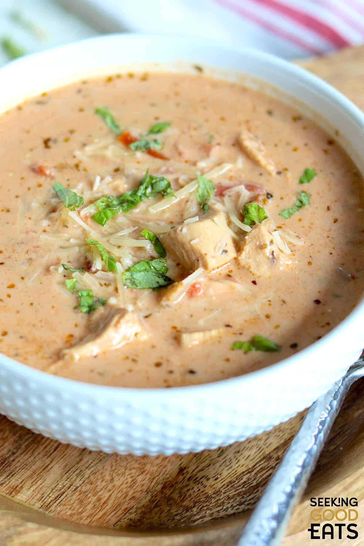 Creamy tomato soup with chicken and canned tomatoes in a white bowl with a spoon.