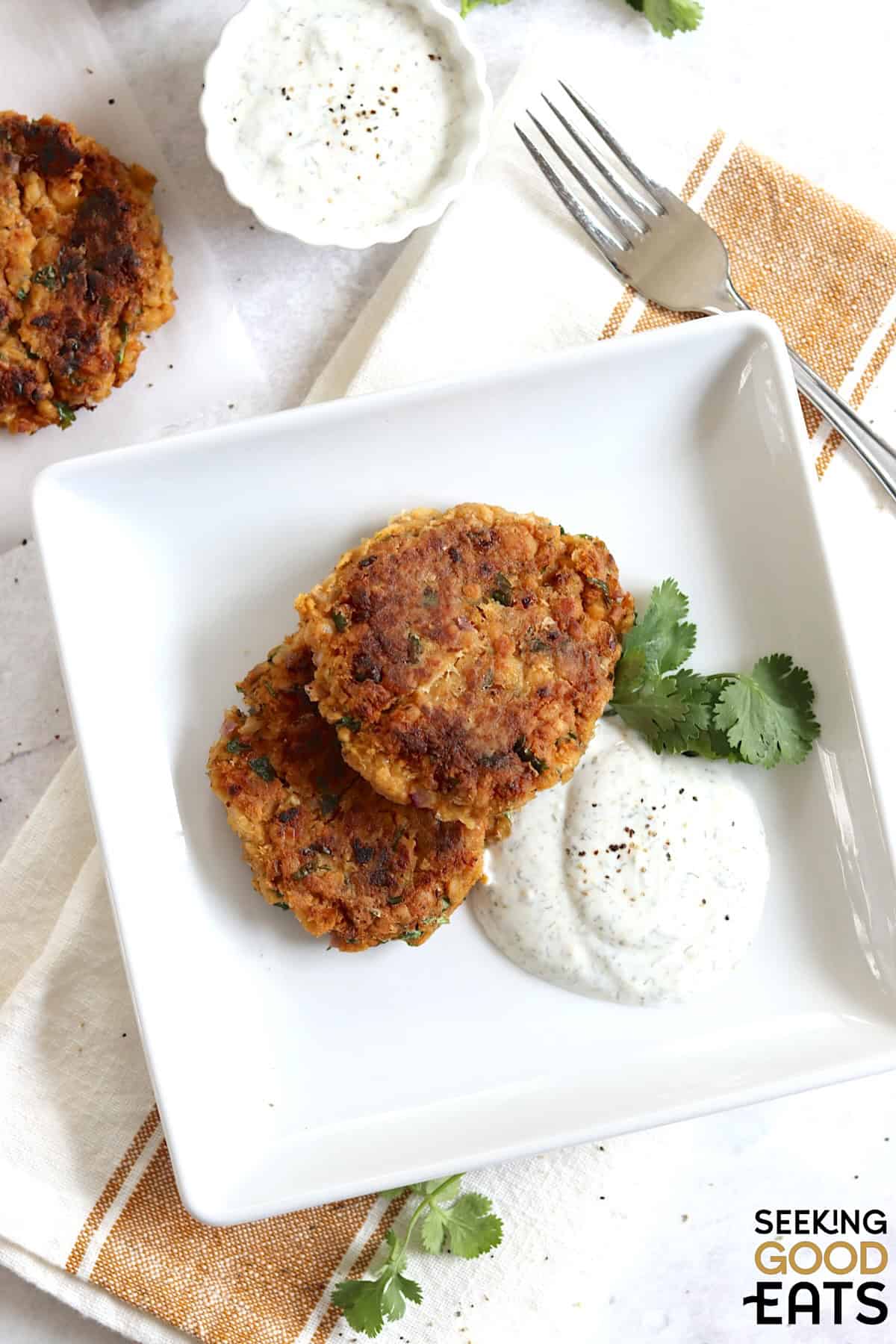 Golden brown chickpea fritters served with creamy dipping sauce on a white plate.