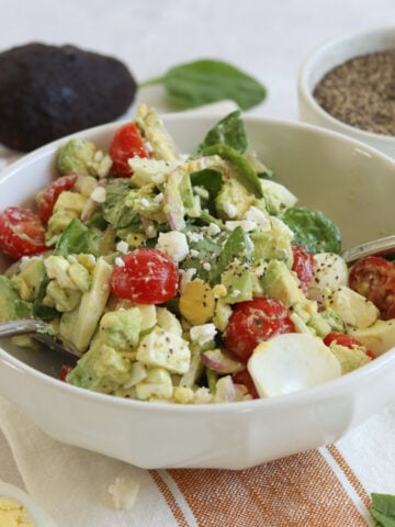 Avocado egg salad in a white bowl and two silver serving utensils.