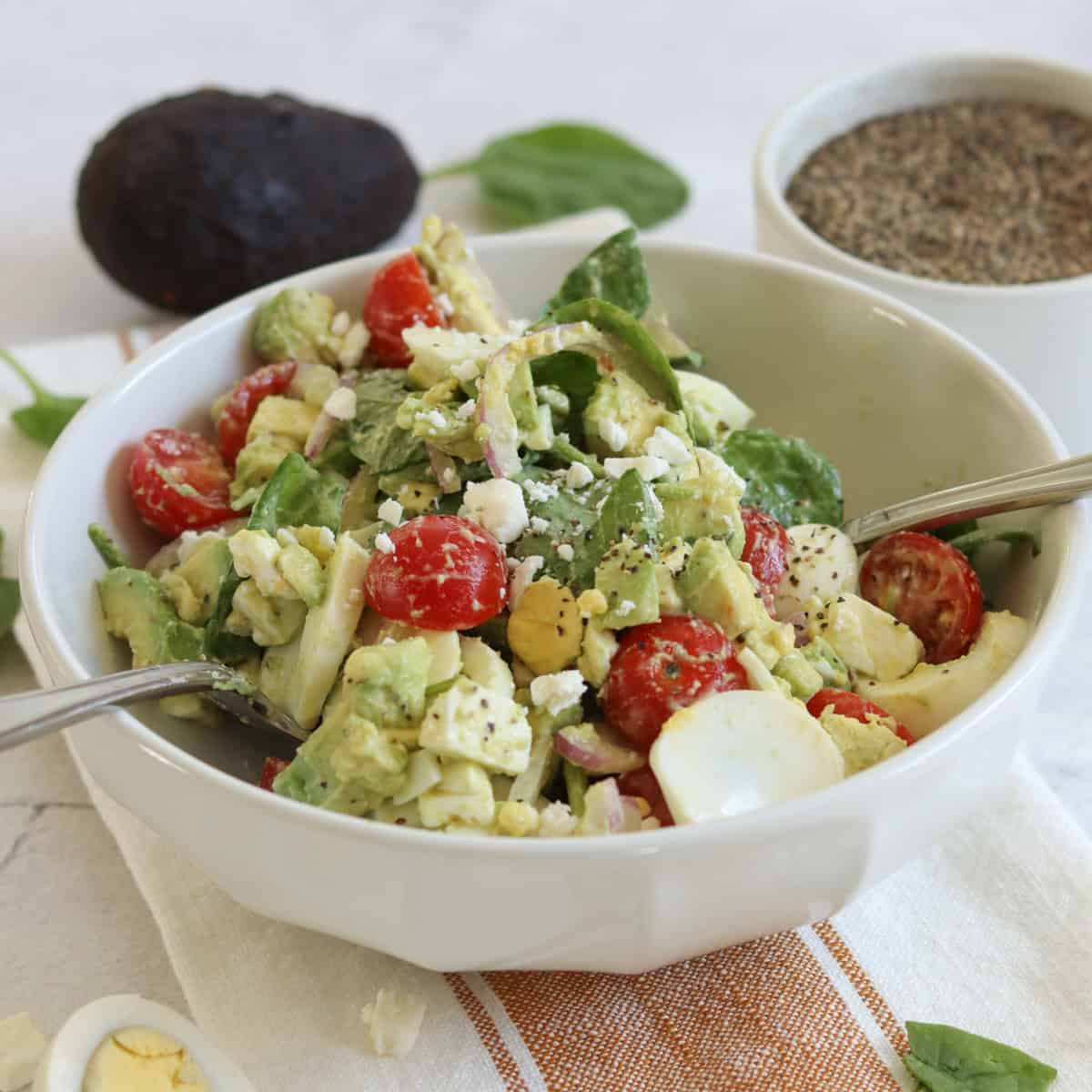 Avocado egg salad in a white bowl and two silver serving utensils.