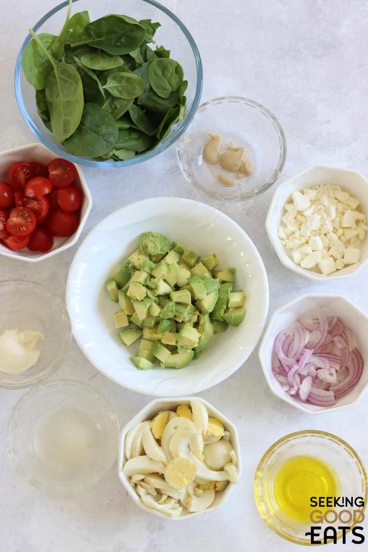 Ingredients needed to make avocado egg salad on a white marble countertop.
