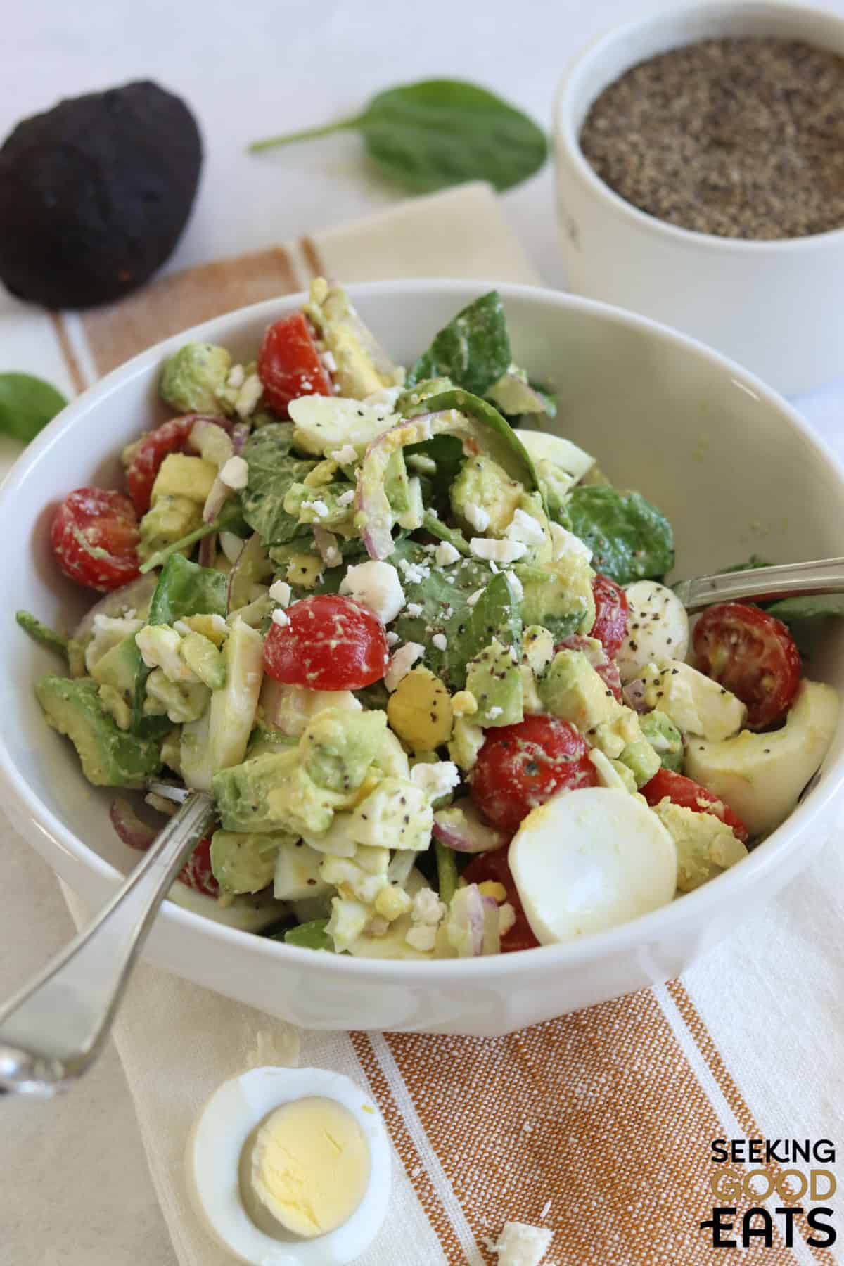 Avocado egg salad in a white bowl and two silver serving utensils.