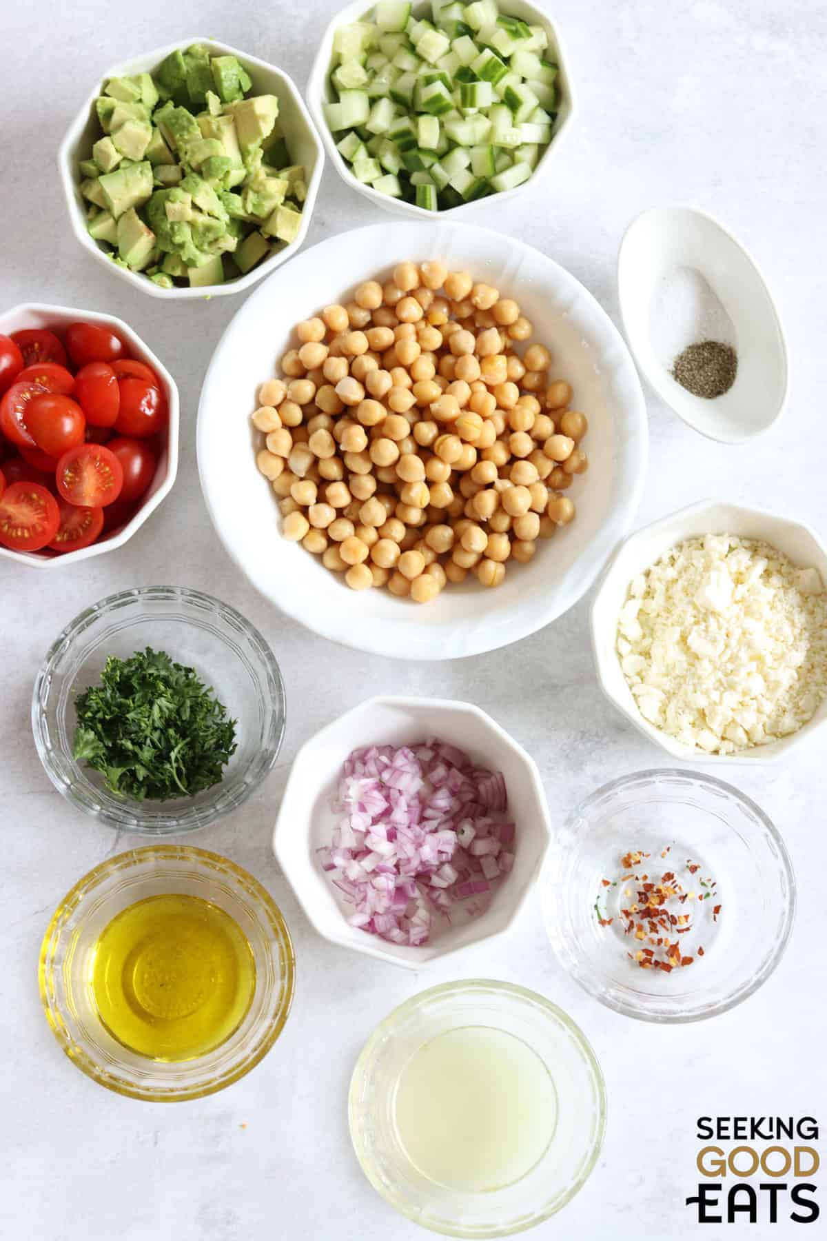 Ingredients needed to make feta avocado chickpea salad on a marble countertop.